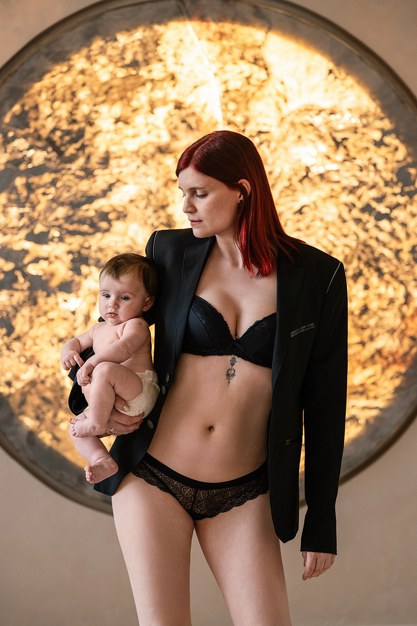Glamour anya-baba fotózás Budapesten, édesanya fekete zakóban tartja karjában kisbabáját.